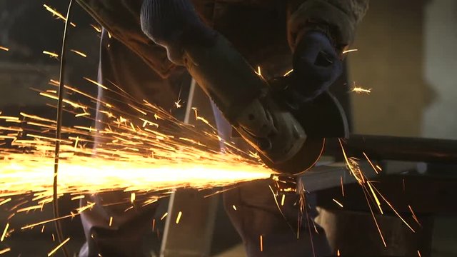 Man with side grinder cutting a long metallic bar with plazma sparkles