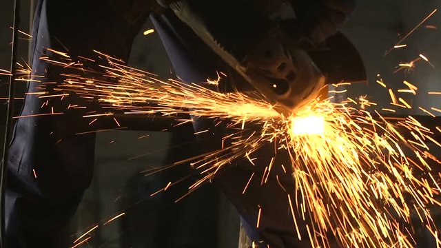 Guy with disc grinder cutting a long metallic billet with plazma sparkles