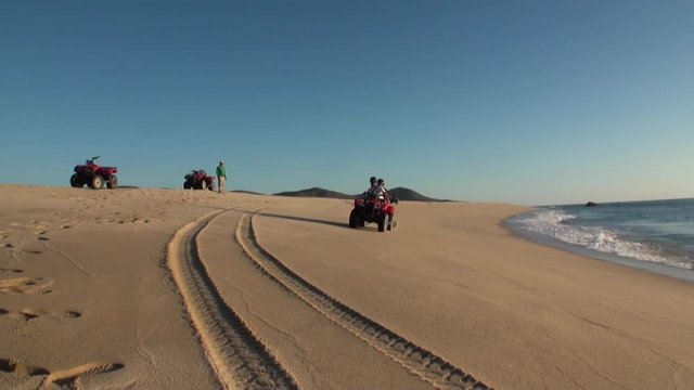 Team of tourists rides quad bike along sandy shore and waving greeting. Concept of outdoor activities and travel.
