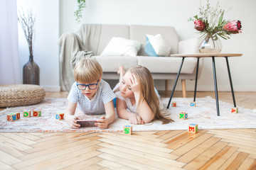 Two kids playing smartphone. Boy and girl at home watching at the cell phone. Digital children...