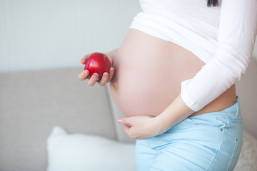 Attractive pregnant woman with apple. Expecting woman holding healthy food. Lady eating an red apple. Proper nutrition for pregnancy.