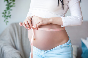 Young pregnant woman indoor. Lady measuring her round stomack. Beautiful woman expecting baby.
