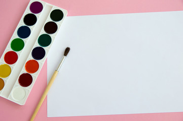 Multi-colored objects for drawing and creativity for children lie on a pink background. Bright watercolor paints, pencils, brushes and markers are on the table. A set for the artist to draw .