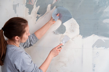 woman tears off Wallpaper, removing Wallpaper from the wall with a spatula, the process of updating the wall room repair. with free text space