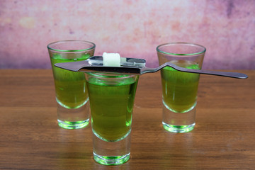 Three glasses with absinthe, a special spoon for absinthe and a piece of refined sugar