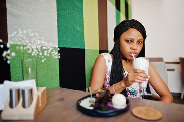 Сheerful african american young woman in summer dress and choker necklace at cafe drinking milkshake.