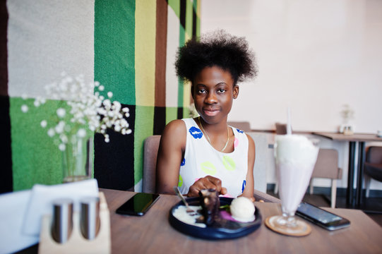 Сheerful african american young woman in summer dress at cafe with milkshake and dessert. - Powered by Adobe