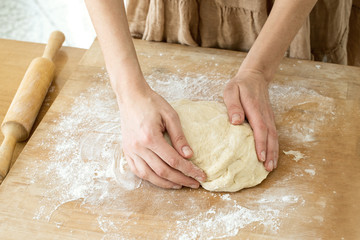 Dough yeast  lying on a wooden cutting board sprinkled with flour, and woman hands.