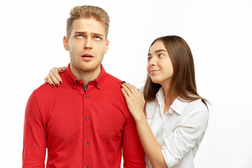 a pretty brunette in a white shirt hugs and reassures her companion - a young man with blond hair who rolls eyes up in horror and fatigue. Studio portrait on isolated white background