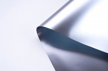 Curled corner of silver or metallic paper on white background