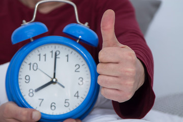 man in bed with alarm clock close up and with thumb raised in ok sign