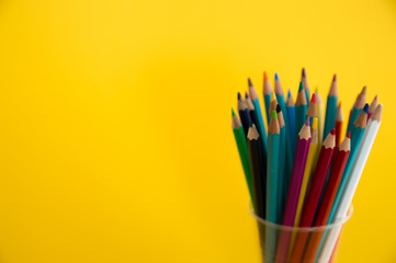 Colored wooden pencils for drawing in a glass stand on a yellow background. Children's multi-colored pencils for drawing.