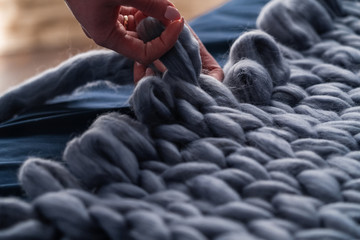 The process of knitting blankets made of Merino. blanket made of natural sheep wool. hand yarn close-up. home produces handmade plaid. designer volumetric blanket. loop weaving knits with bare hands