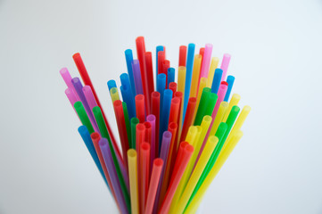 Multicolored plastic tubules for a cocktail in a glass on a white background. Polymers in everyday life.