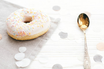 Delicious  white donut with colorful sprinkles  on stylish white table with confetti and vintage spoon. Party concept. No diet. Candy bar at wedding reception.