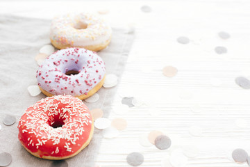Delicious colorful donuts with sprinkles on stylish  white table with confetti, copy space. Party concept. No diet. Candy bar at wedding reception. Purple, pink, white donuts