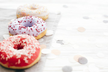 Delicious colorful donuts with sprinkles on stylish white table with confetti, copy space. Party concept. No diet. Candy bar at wedding reception. Purple, pink, white donuts