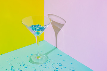 Cocktail glass with funny blue liquid and confetti. Strong fashion shadows. Creative concept of luxury relax with beverage on the beach.  Minimalism