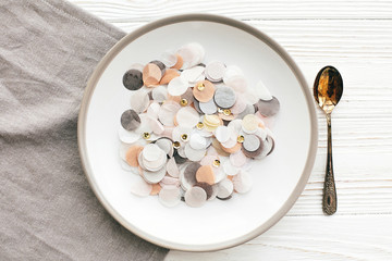 Fototapeta na wymiar Stylish plate with golden confetti and vintage spoon on napkin on white table, flat lay. Modern set, serving for reception and celebration. Party and diet concept