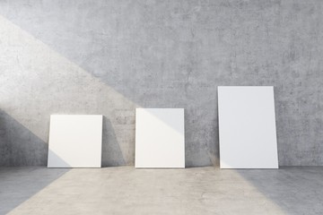 three clean canvases of different sizes stand near the concrete wall