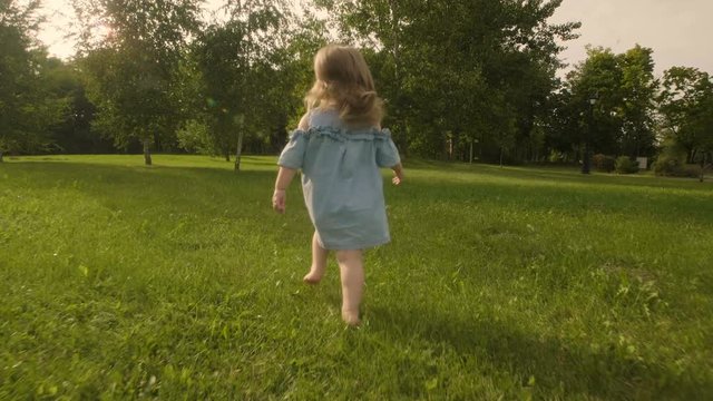 Baby girl running through the grass in garden in sunset sunlight. Slow motion. Happy smiling baby girl.