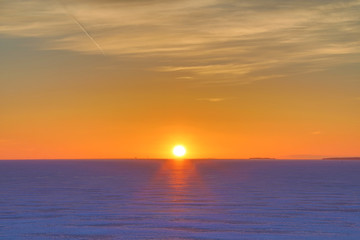 Obraz premium The sunset or sunrise. The cloudy sky cloured in red, orange, crimson, purple, violet and blue bright and vivid coloures with setting or rising sun over the sea, lake or bay covered with ice and snow
