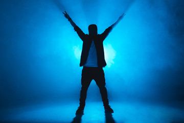 Fototapeta na wymiar Sporty modern style hip-hop dancer dressed in urban style wear shows his dance on blue studio background.