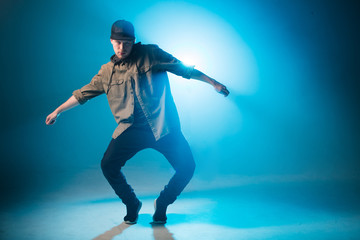 Sporty modern style hip-hop dancer dressed in urban style wear shows his dance on blue studio background.