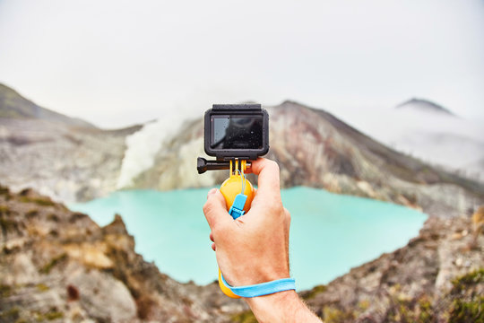 A man takes a picture of a volcano crater on a gopro.