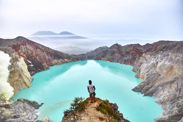 The man stands on top of the volcano and looks at the lake in the crater. © Dima Anikin