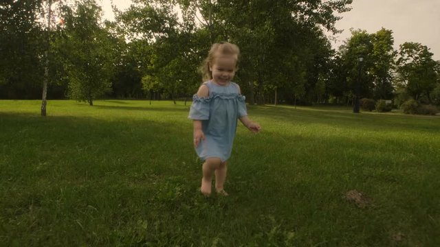 Baby girl running through the grass and rushes into mother hands in garden in sunset sunlight. Slow motion. Happy smiling baby girl.