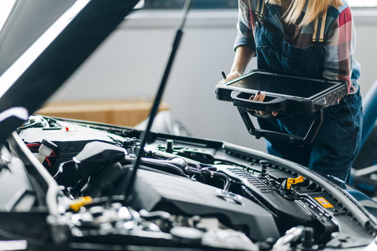 closeup photo. female mechanic holding a scanner while standing behind the hood. close up cropped photo
