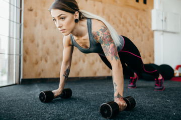 Fototapeta na wymiar Gym woman doing push-up exercise with dumbbell