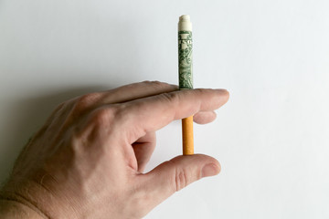 A hand is holding a cigarette rolled into a dollar bill. Smoker's hand holds  cigarette hidden in paper money.