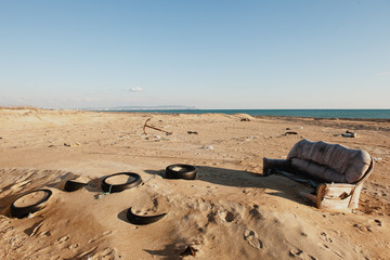 dirty deserted beach and an old sofa against the backdrop of the sea ecological disaster