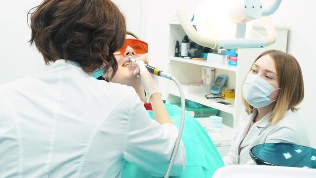 Close-up of medical dentist team in dental office making a teeth cleaning to female young patient. Dental care.