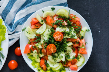 Fresh spring vegetable salad from tomato and cucumber on a black background, close up.