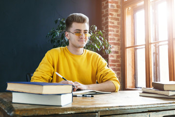 Fototapeta na wymiar Young serious blonde man wearing glasses and yellow pullover studying or working in the class