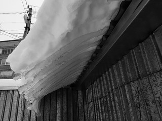 Dangerous ice block with snow on the roof hangs in the winter