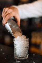 Battender hand adding ice chips in empty cocktail glass, close up. Barman at work in the restaurant. class with ice in focus.