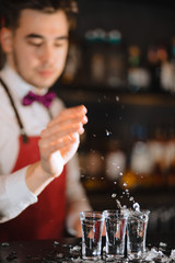 Bartender in the white shirt and red apron adding ice crumbs into an empty cocktail glass on the bar counter at restaurant