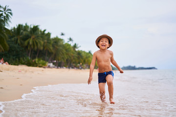 A child in a hat runs and smiles - Asian boy in a hat, blurred background
