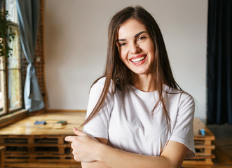 Portrait of brunette longhaired cheerful woman wearing white t-shirt smiling at the studio