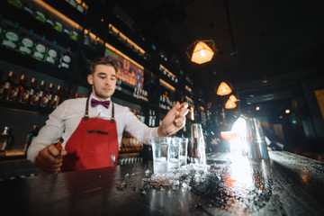 Low angle shot of bartender putting some ice into shot frosted glasses on a wooden counter.