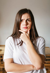 Fototapeta na wymiar Portrait of brunette longhaired woman wearing white t-shirt thinking about something with serious emotion