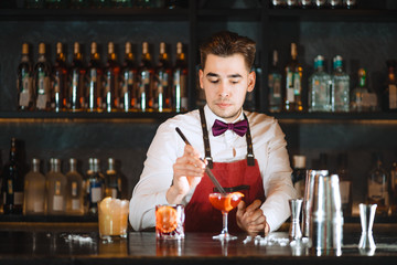 Bartender finishing his cocktail with orange peel zest slice using long tweezers
