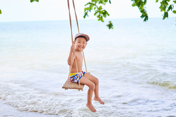 The boy is riding on a swing, on the background of the ocean