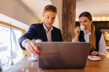 A stylish couple drinks morning coffee at the cafe and works with a laptop, young businessmen and freelancers