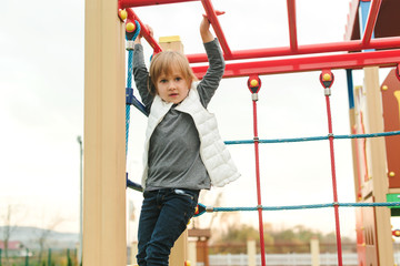 Cute little girl playing on climbing net at school yard playground. Kid play and climb outdoors. Happy child playing at preschool sport center. Modern rope web playground outdoor