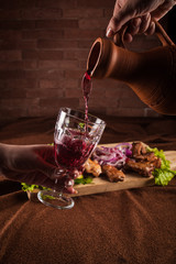 Red wine is poured from a clay jug into a glass goblet